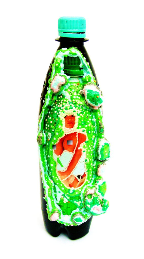 Plastische Kunst von Künstler Nede (Peter Debusi) aus der Serie „Flaschenpost“. Das Objekt vor weißem Hintergrund besteht aus einer großen, aufrecht stehenden, dunkelbraunen Kunststoffflasche mit einem hellblauen Schraubverschluss. In den Bauch dieser Flasche ist eine zweite, kleinere grüne Kunststoffflasche hineingearbeitet, deren eigener grüner Deckel im oberen Bereich sichtbar ist. Die Vorderseite ist reliefartig mit einer organischen, leuchtend grünen Masse verziert, die mit kleinen weißen Perlen und pinkfarbenen Elementen besetzt ist. Dieser reliefartige Rahmen umschließt die im Zentrum der inneren Flasche eingearbeitete Fotografie einer nackten Frau, die mit einer Perlenkette verziert ist.